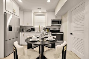 Una cocina moderna con armarios blancos, un refrigerador de acero inoxidable, un microondas y una mesa de comedor preparada para cuatro.