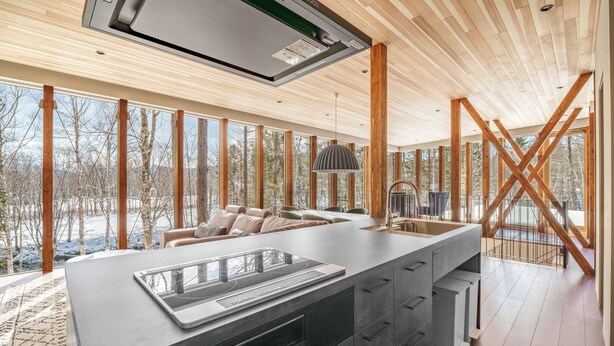Une cuisine moderne dotée d’un grand îlot central, de poutres en bois et offrant une vue sur un paysage enneigé.