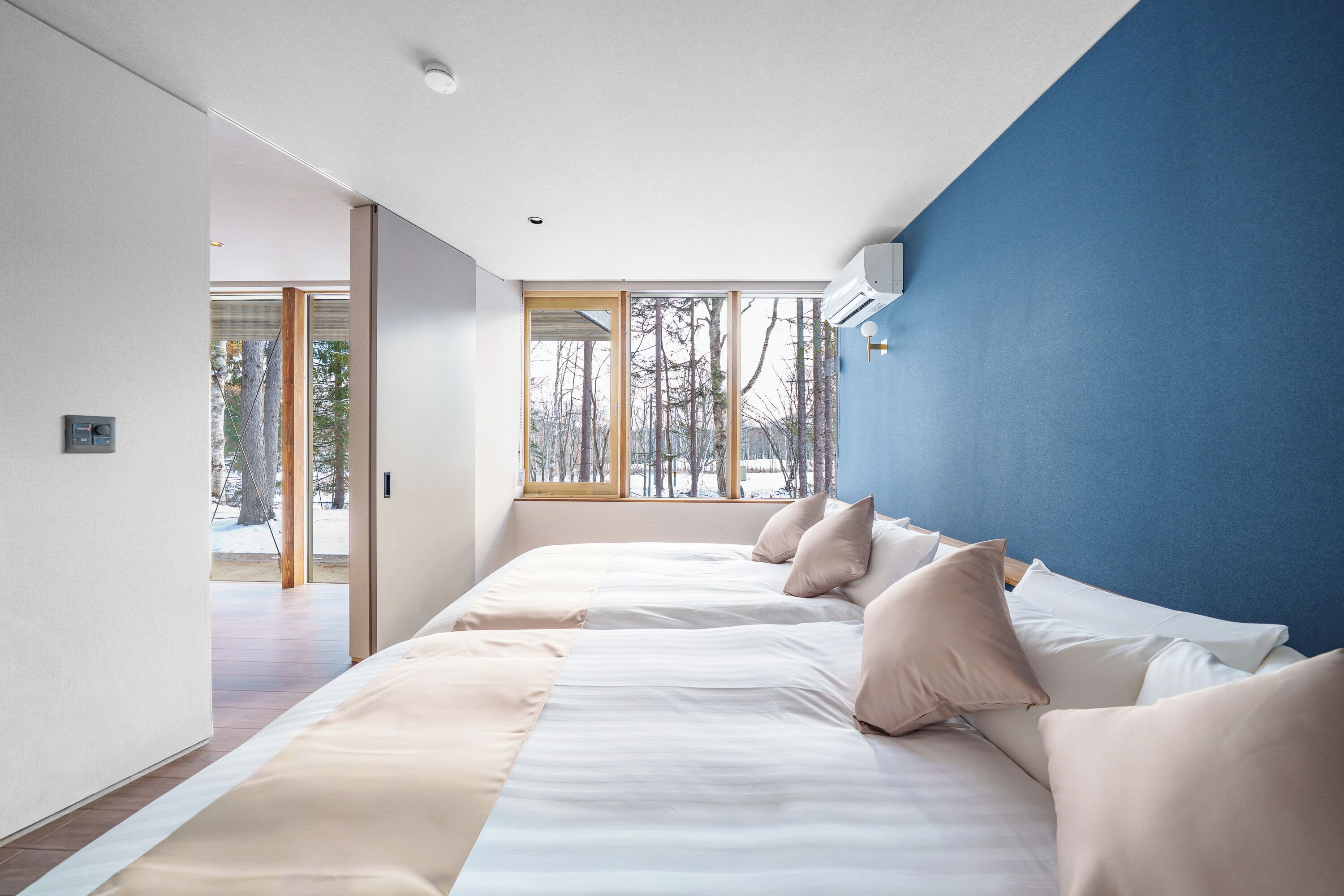 A modern bedroom with a large bed, a blue accent wall, and a view of trees through the window.
