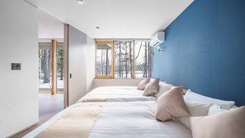 A modern bedroom with a large bed, a blue accent wall, and a view of trees through the window.