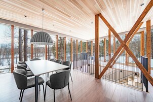 Un interior moderno con techo de madera, ventanas amplias, una mesa de comedor y sillas.