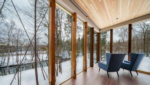 Une pièce spacieuse avec de grandes fenêtres, un plancher en bois et deux chaises bleues.