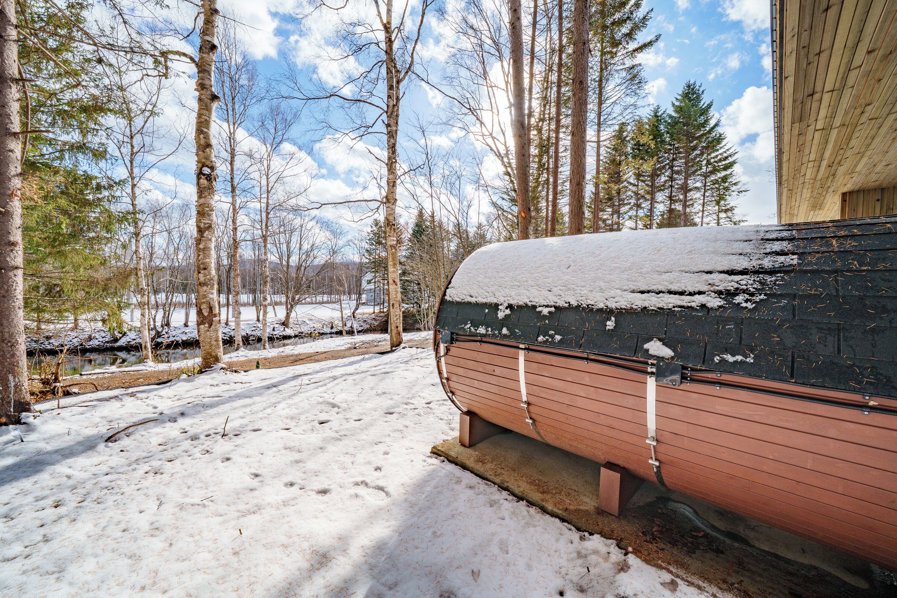 A snow-covered landscape with a wooden structure, possibly a cabin or house, surrounded by trees.