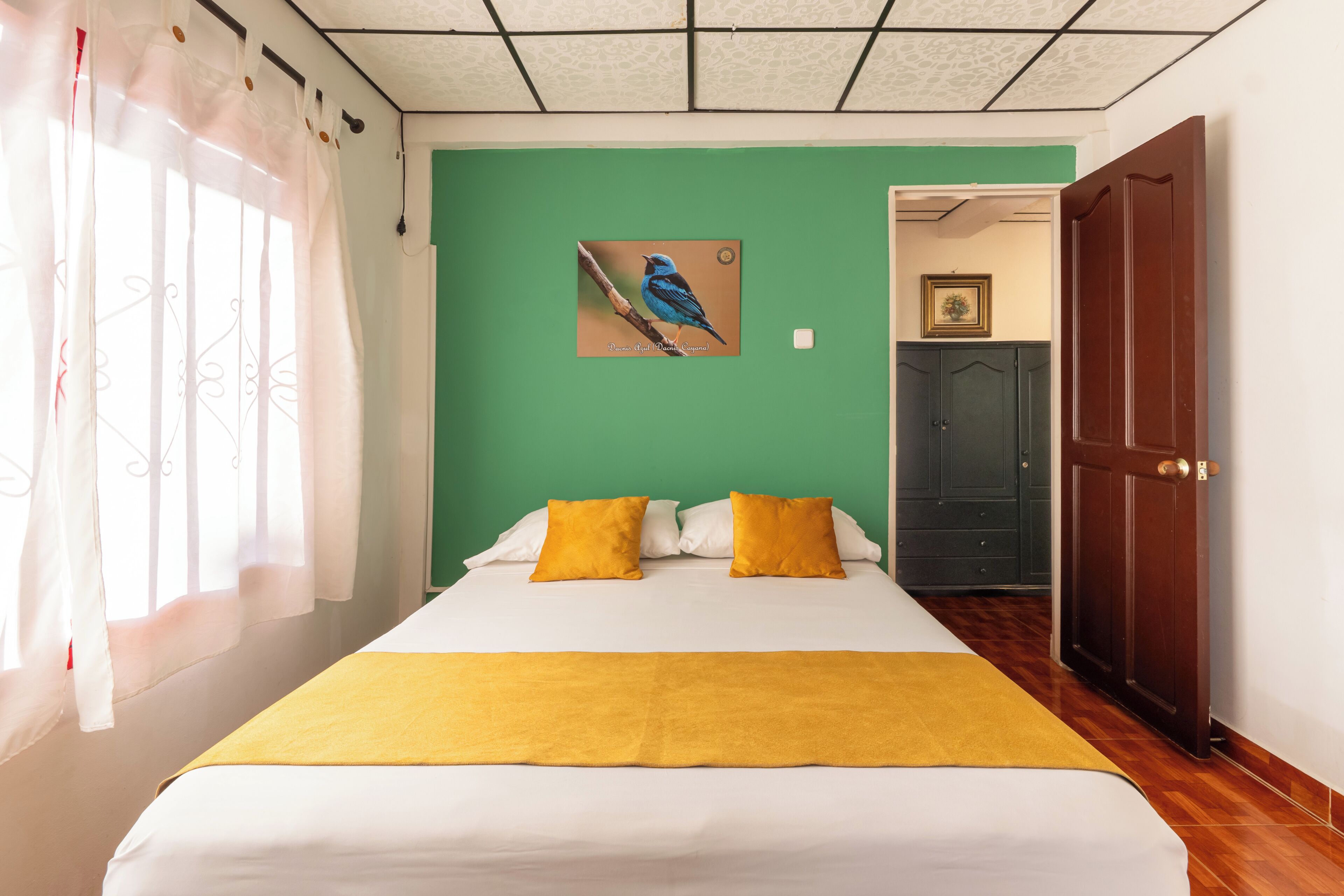 Un dormitorio con una cama, paredes verdes, una ventana con cortinas, una puerta y un cuadro en la pared.