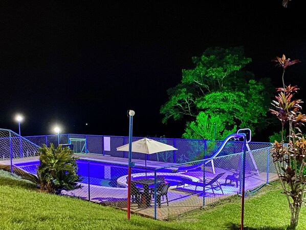 An outdoor swimming pool area with a fence, a covered seating area, and a large tree in the background. - Finca Hotel Resplandor Quindiano (Circasia)