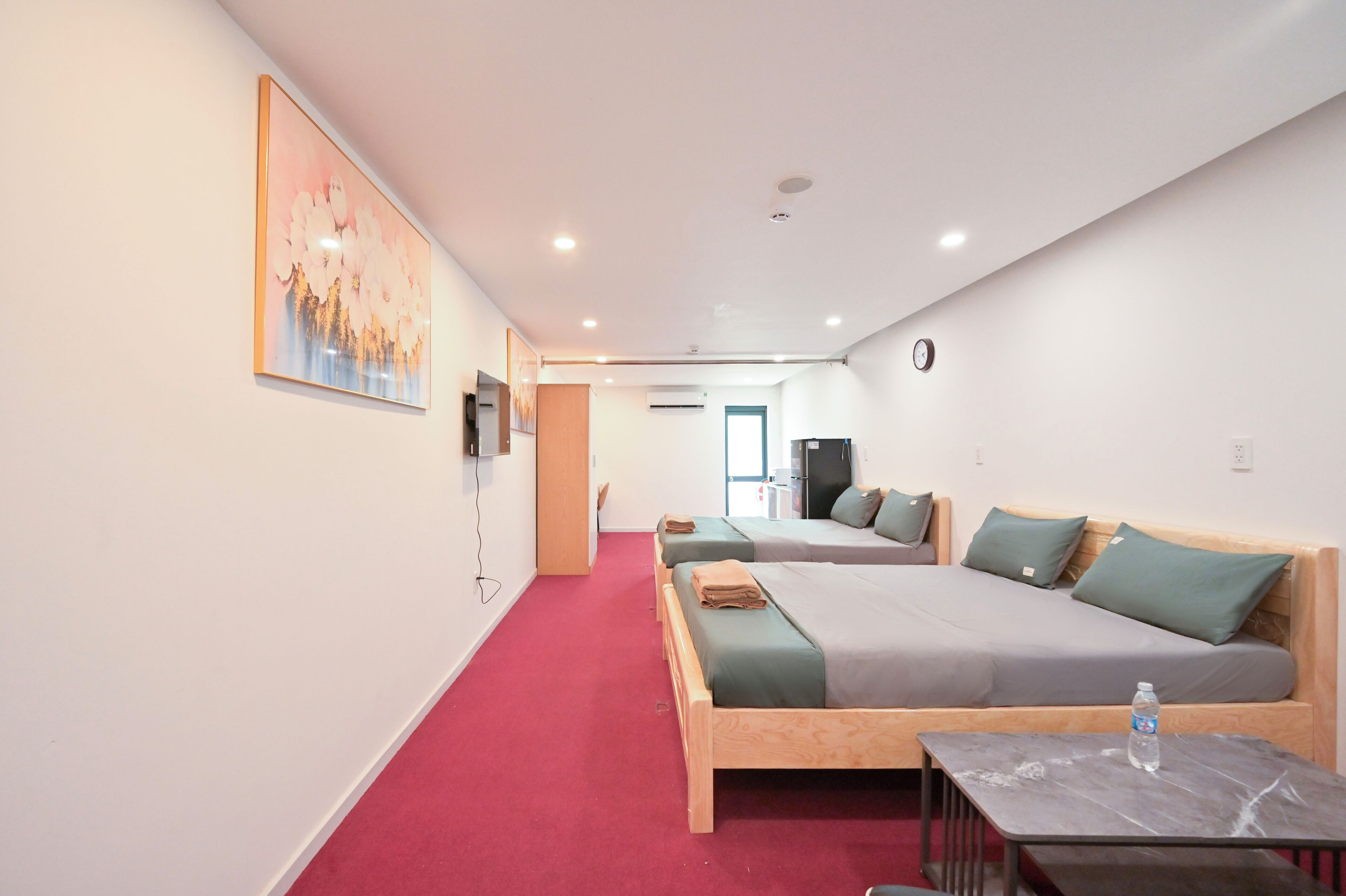 Ein Hotelzimmer mit zwei Betten, einem roten Teppich, einem Gemälde an der Wand und einer Wasserflasche auf dem Tisch.