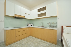 Una cocina compacta con armarios blancos, una campana extractora de acero inoxidable, un microondas y un lavabo.