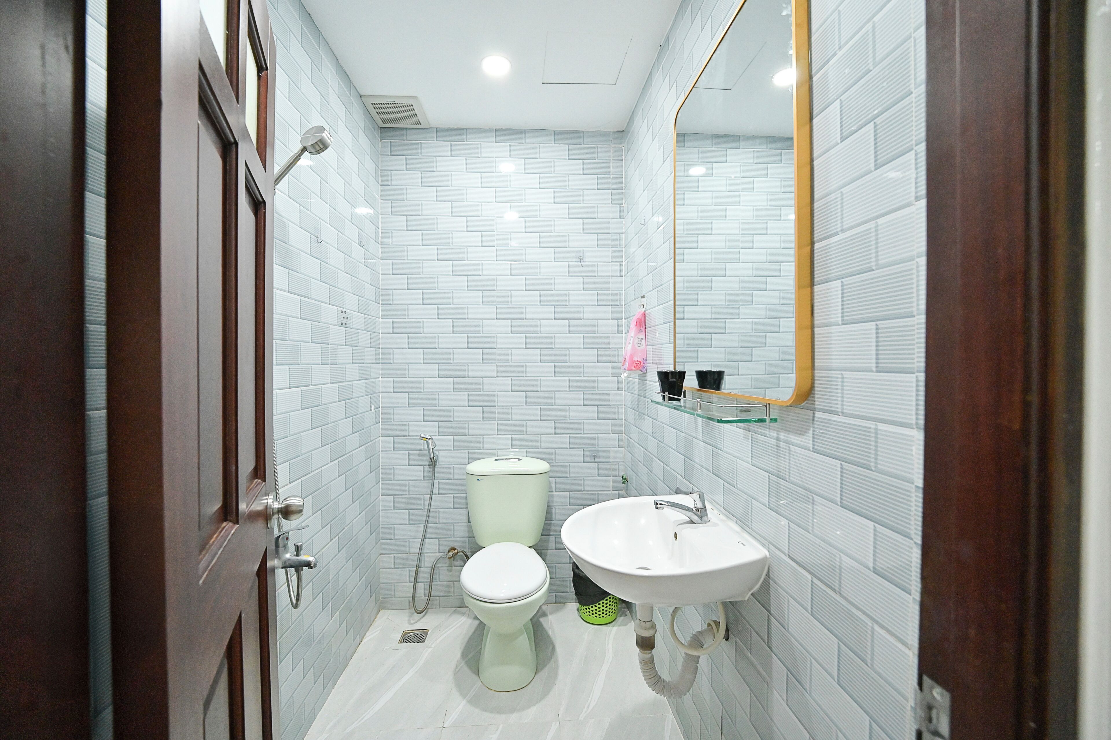 Un baño con paredes de azulejos blancos, un inodoro blanco, un lavabo y un espejo.