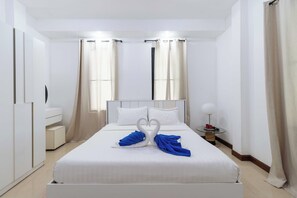 Hotellihuone, jossa on sänky, verhot, yöpöytä ja vaatekaappi.