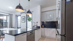 Una cocina moderna con armarios blancos, encimera negra, electrodomésticos de acero inoxidable e iluminación colgante.