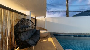 Zona junto a la piscina con una silla de mimbre, una mesita redonda y una pared de bambú.