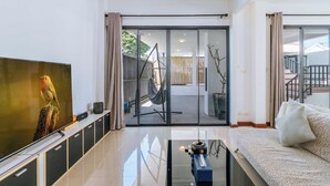 Una sala moderna con una televisión de pantalla plana, un sofá, una mesa de centro y un ventanal corredero que da a un balcón.