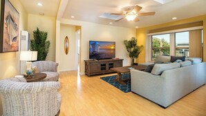 A living room with a sofa, armchairs, a TV, a ceiling fan, and a large window. - Block to Beach Family Home w/ King Bed, Jacuzzi & BBQ (San Diego)