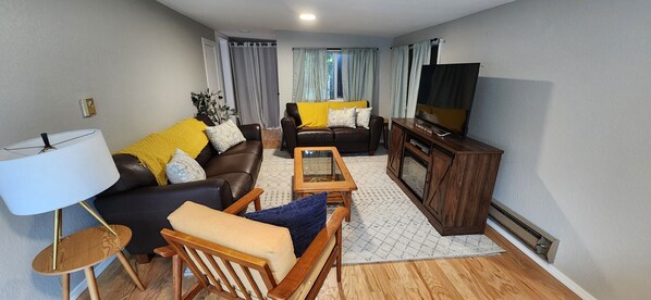 Una sala de estar con sofá, sillón, mesa de centro, mueble para televisión y lámpara.