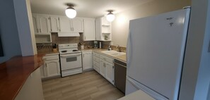 A compact kitchen with white cabinets, a built-in oven, a dishwasher, and a refrigerator.