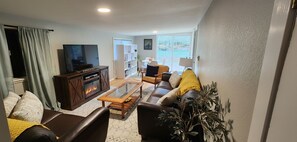 A living room with a fireplace, a television, a sofa, a coffee table, and a view of the outdoors.
