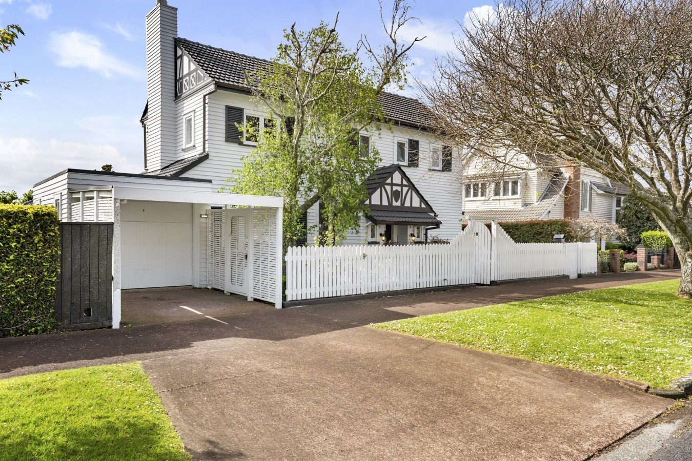 A two-story house with a garage, a white fence, and a driveway.