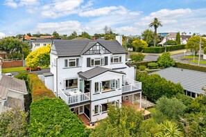 Une maison à deux étages dotée d’un balcon, entourée d’une végétation luxuriante et sous un ciel dégagé.