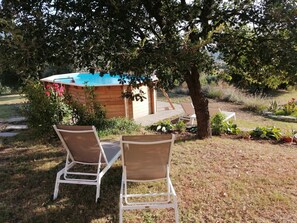 Eine Holzterrasse mit Pool, umgeben von üppiger Vegetation und zwei weißen Liegestühlen.