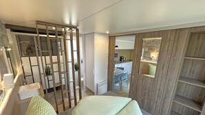 A modern bedroom with a bed, bedside tables, and a view into the kitchen area.