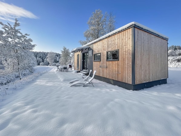 A wooden cabin with a covered patio, snow-covered trees, and a clear sky.
