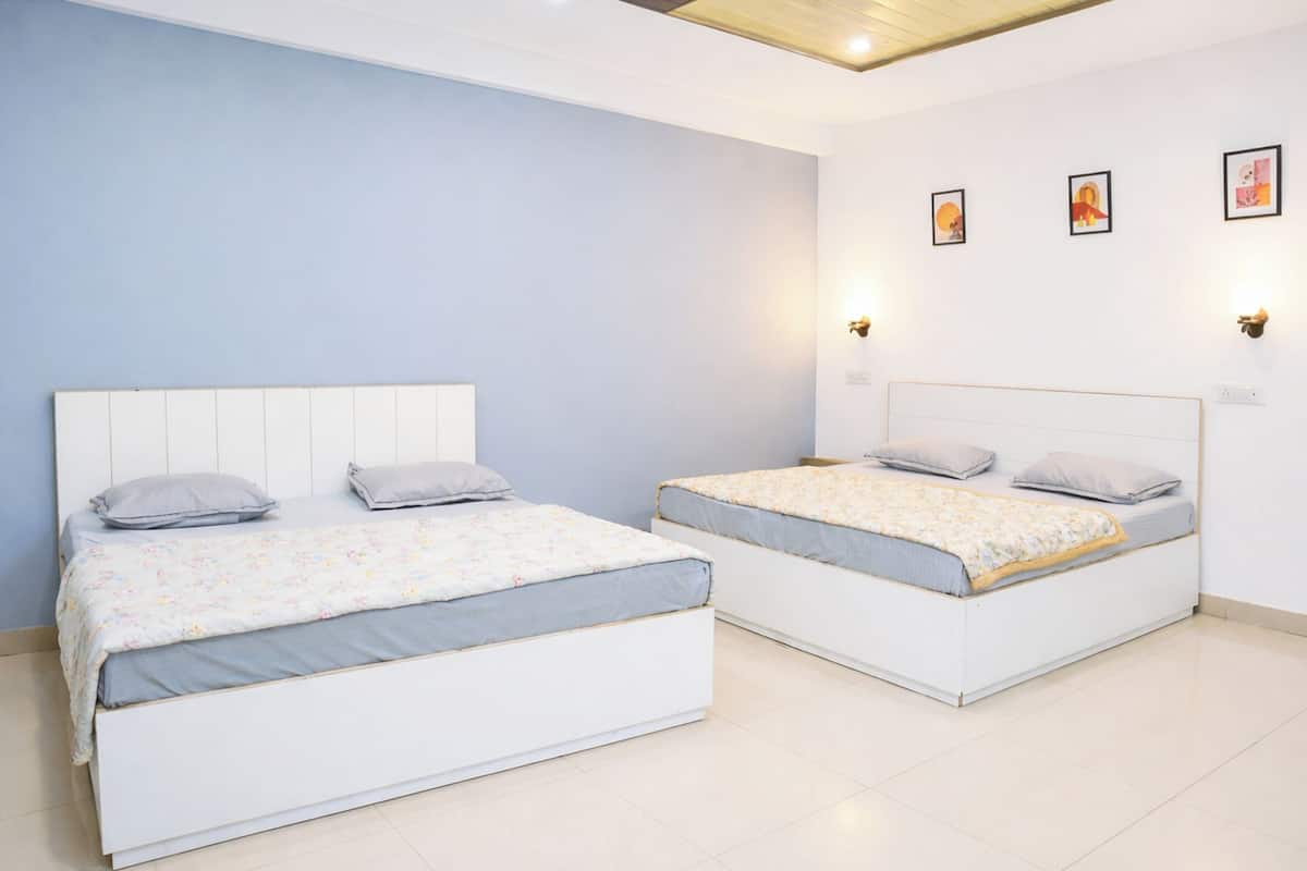 A bedroom with two beds, a light blue wall, and three wall-mounted lights.