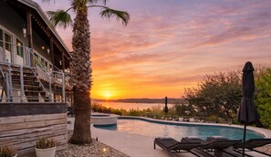 Ein Pool mit Liegestühlen, einer Palme und Blick auf den Sonnenuntergang.
