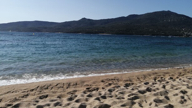 Una spiaggia con acque cristalline, una costa sabbiosa e una montagna sullo sfondo.