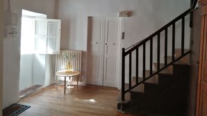 Una stanza con pavimento in legno, una porta bianca, un piccolo tavolo con un vaso e una scala con ringhiera nera.