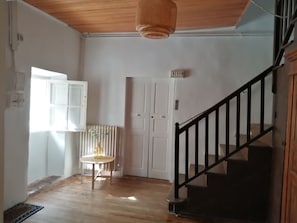 A room with a wooden floor, a white door, a small table with a vase, and a staircase with a black railing. - Olmeto 10 mn plage App 5-6P (Olmeto)