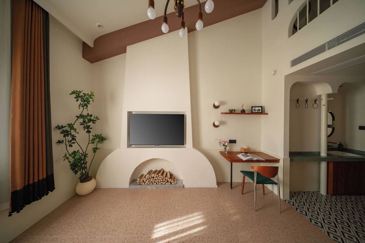 Una sala de estar con chimenea, un televisor de pantalla plana, una mesa de comedor con sillas, una planta en maceta y una zona de cocina con pileta y utensilios.