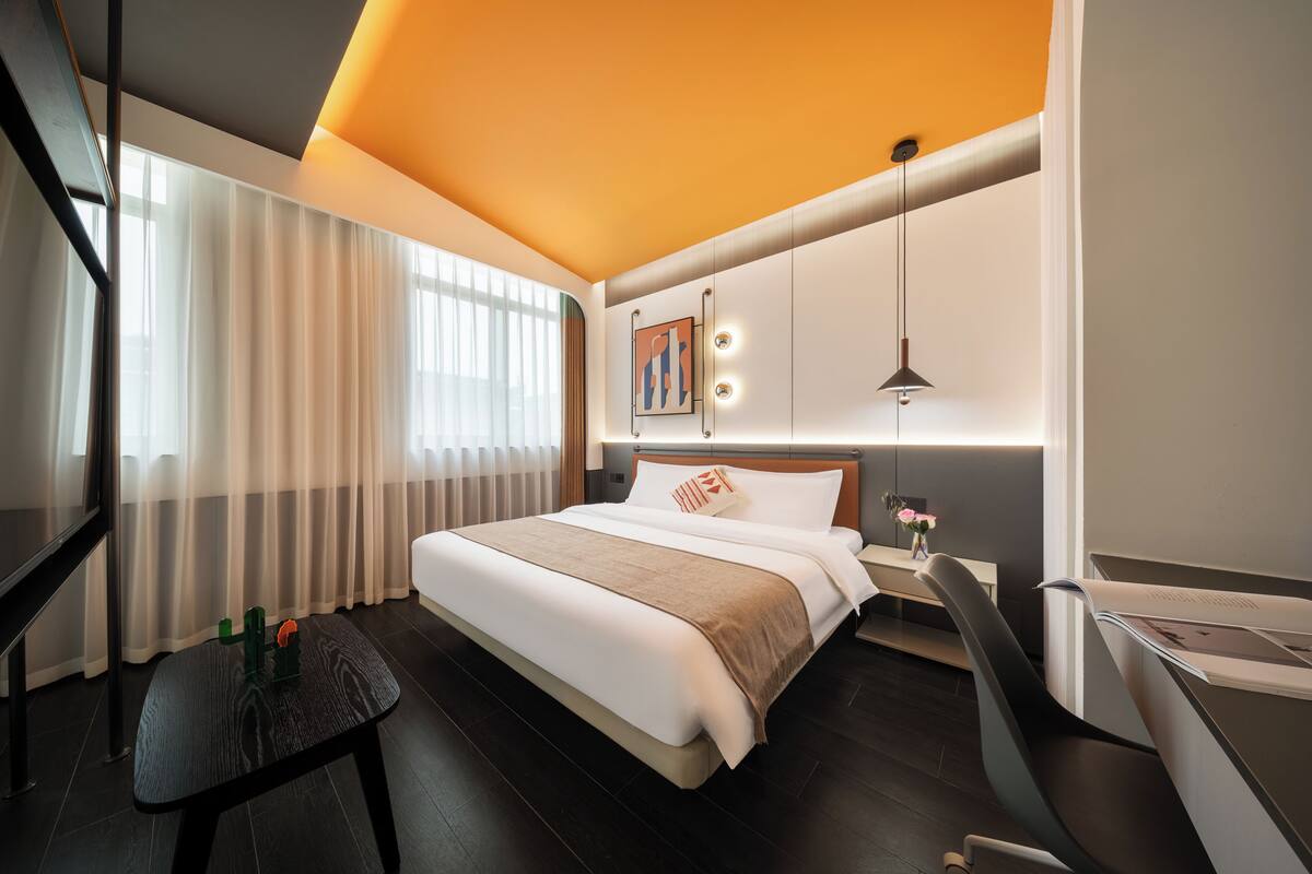 Una habitación de hotel moderna con cama, mesita de noche, escritorio, silla y un gran ventanal con cortinas.