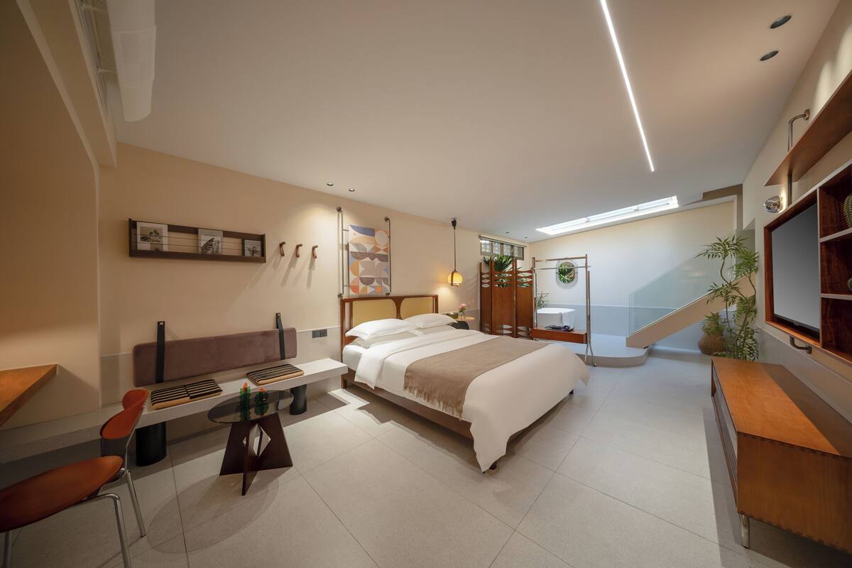 Una habitación de hotel moderna con una cama, un escritorio, una silla, una mesita y una escalera que lleva a un nivel superior.