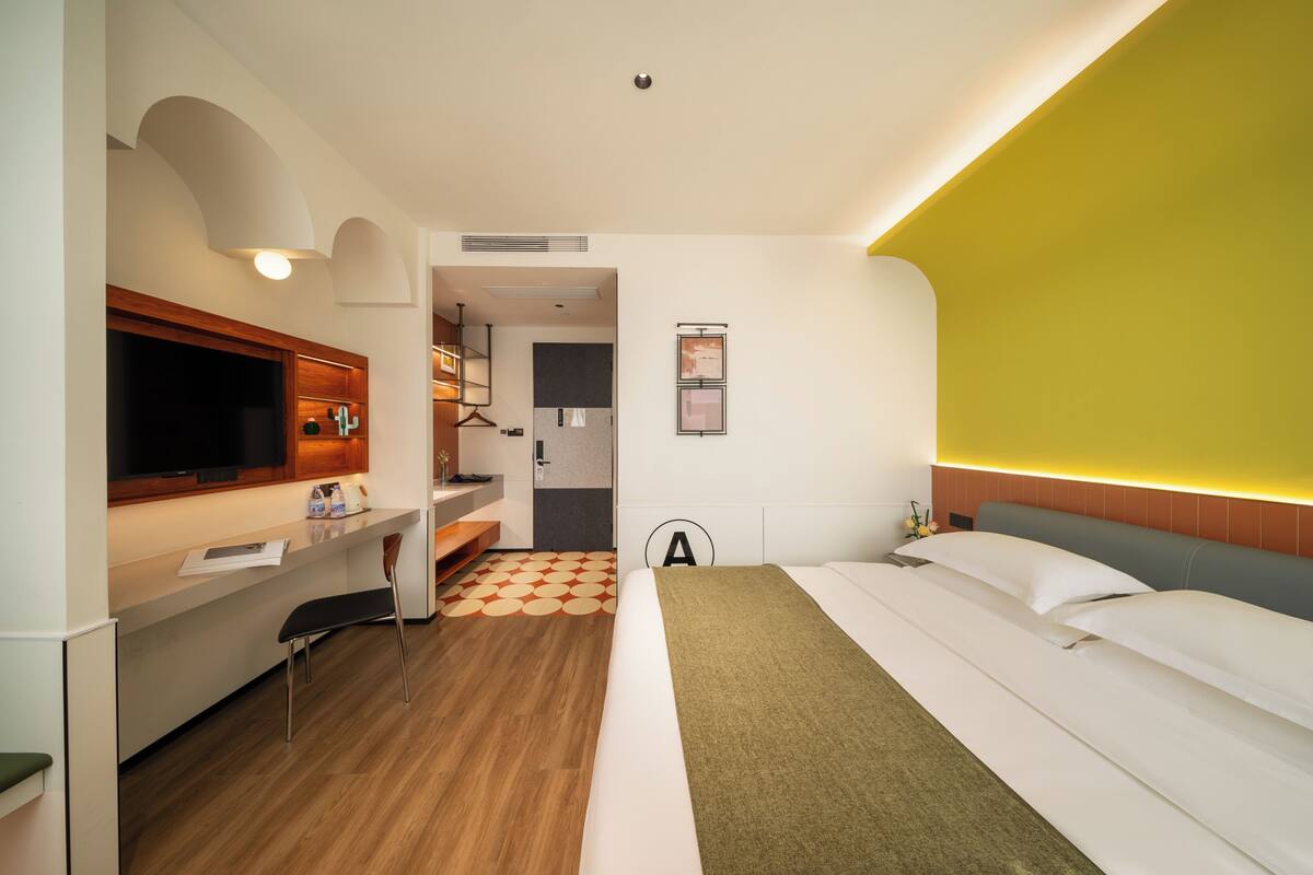 Una habitación de hotel con cama, escritorio, televisor y baño visible a través de una puerta abierta.