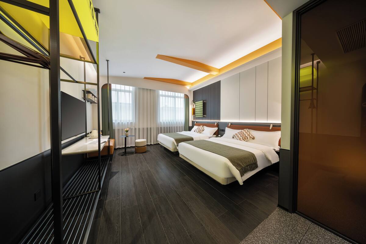 Habitación de hotel moderna con dos camas, un escritorio, una silla, una mesita y una ventana con cortinas.