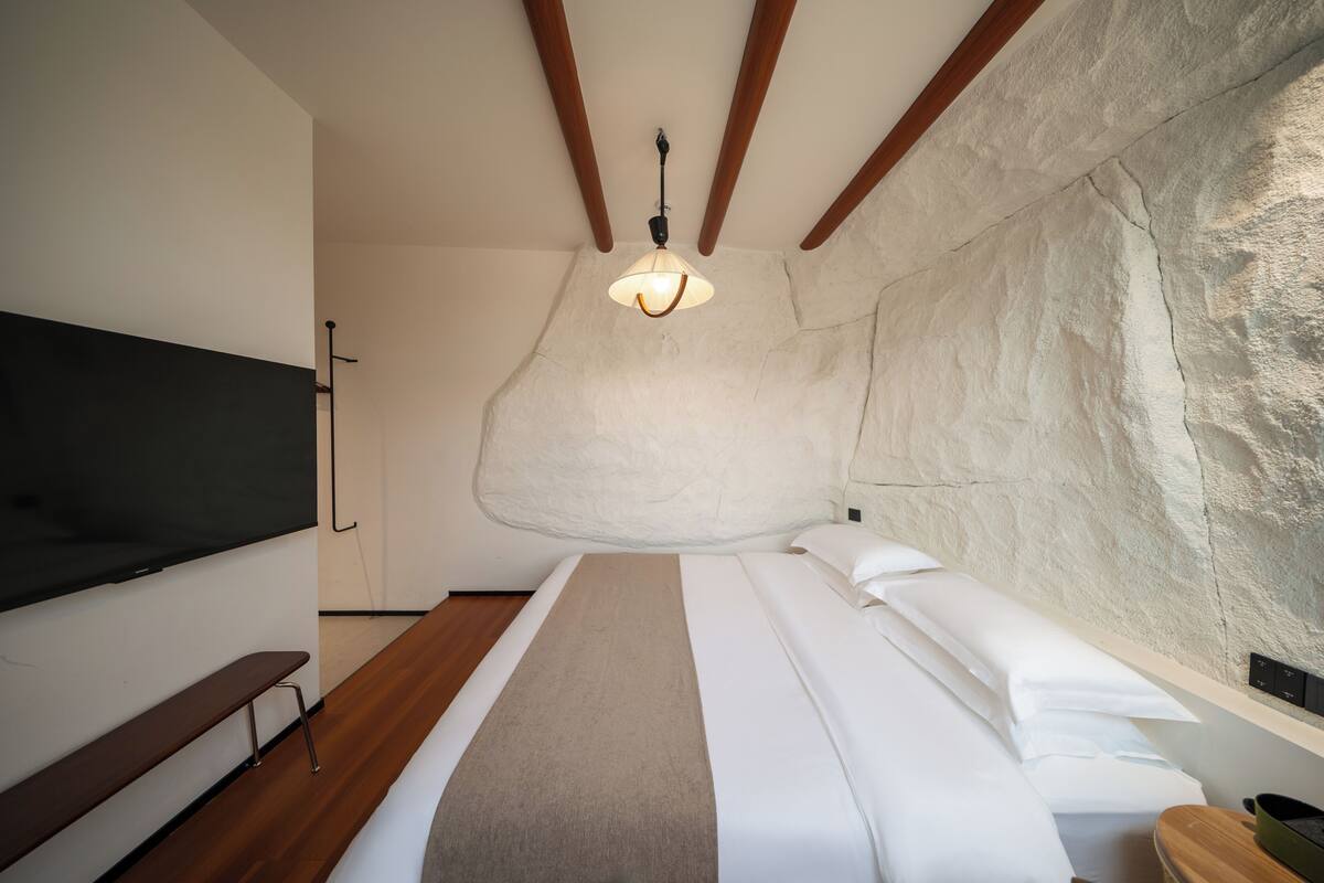 Un dormitorio con una cama, un banco, un televisor y una pared de piedra.