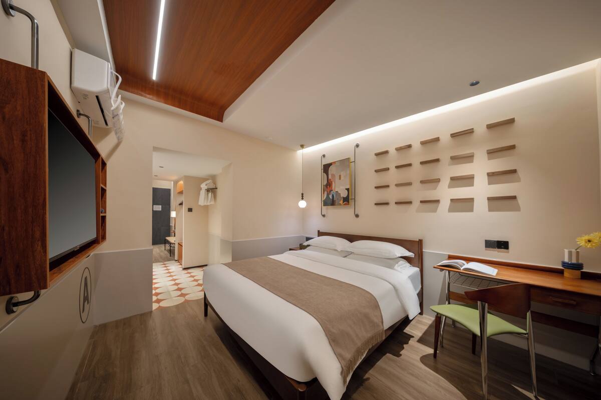 Una habitación de hotel con cama, escritorio, silla y televisor montado en la pared.