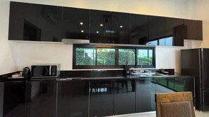 A modern kitchen with black cabinetry, a microwave, and a window overlooking greenery.