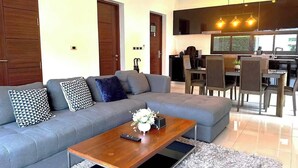 A modern living room with a grey sofa, a wooden coffee table, and a dining area with chairs and a table.