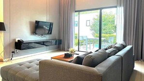 A modern living room with a sofa, a coffee table, a flat-screen TV, and a large window with curtains.