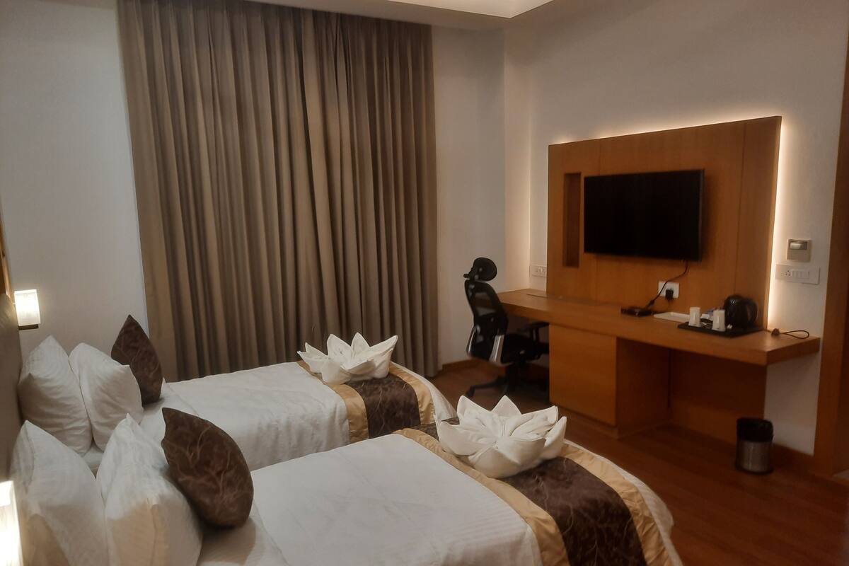 Ein Hotelzimmer mit zwei Betten, einem Schreibtisch, einem Sessel, einem Fernseher und einem Vorhang.
