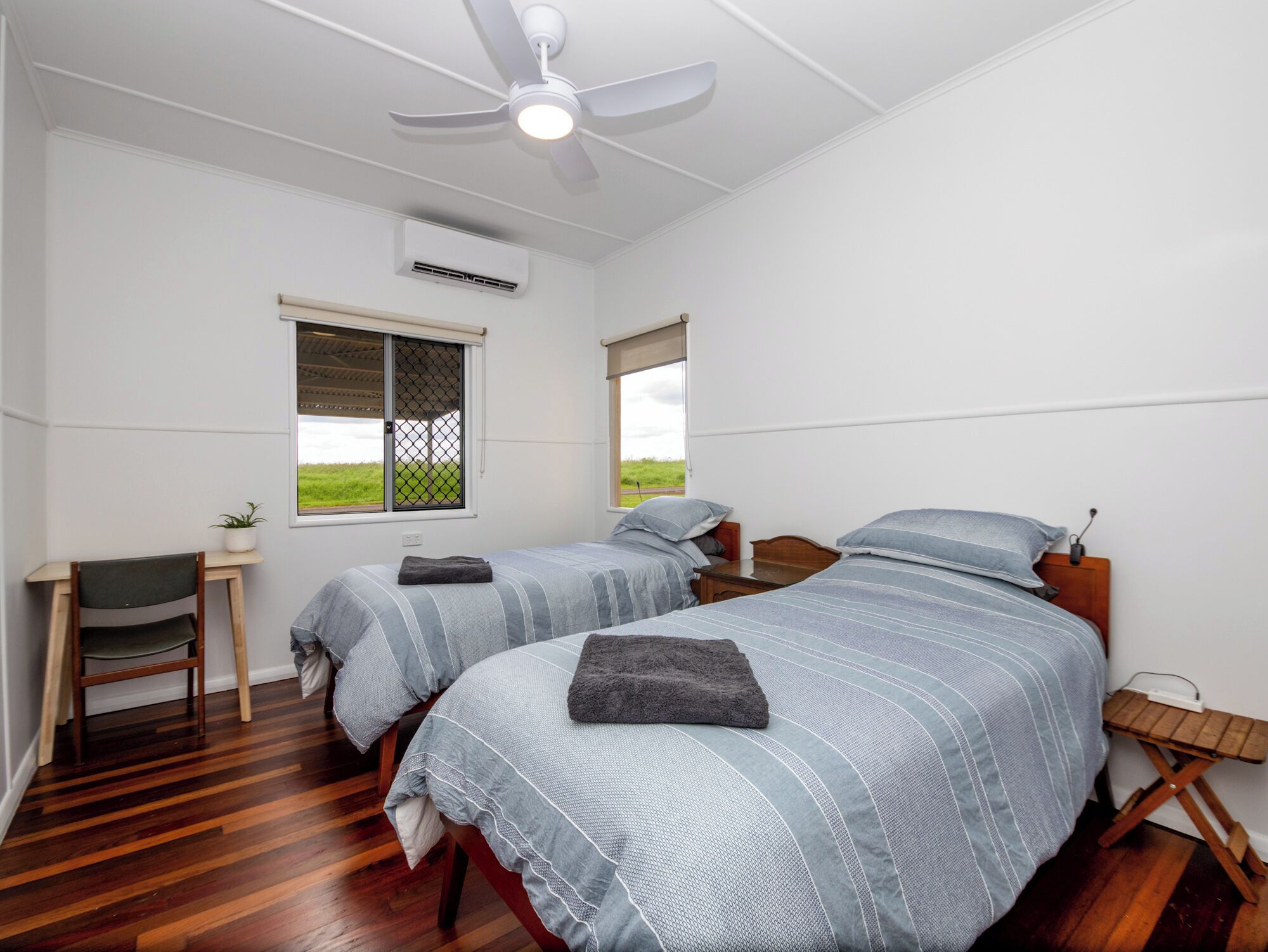 A bedroom with two beds, a ceiling fan, an air conditioning unit, a desk, and a chair.