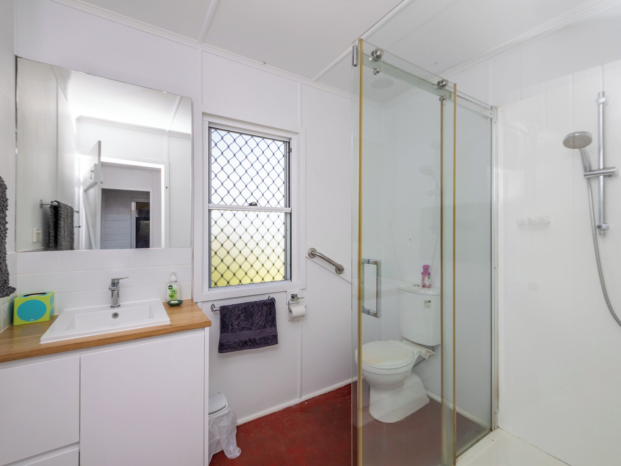 Une salle de bain avec un lavabo blanc, un miroir, des toilettes et une douche à parois de verre.