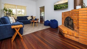 A living room with a blue sofa, wooden coffee table, blue bean bags, a fireplace, and a ceiling fan. - Large family home in a quiet rural location. (Isis Central)