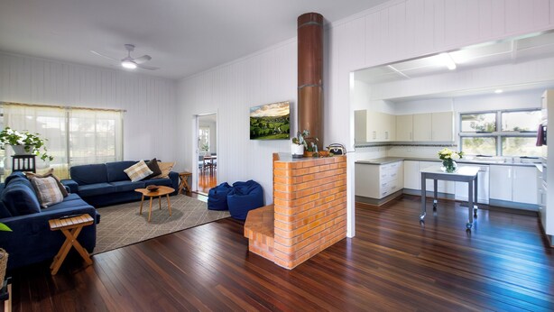 A modern living room with a brick fireplace, a sofa, and a dining area. - Large family home in a quiet rural location. (Isis Central)