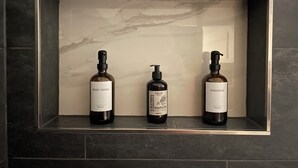 A bathroom shelf with three bottles of body wash and shampoo. - PAULINEN Residence - Live comfortably - Arrive flexibly (Detmold)