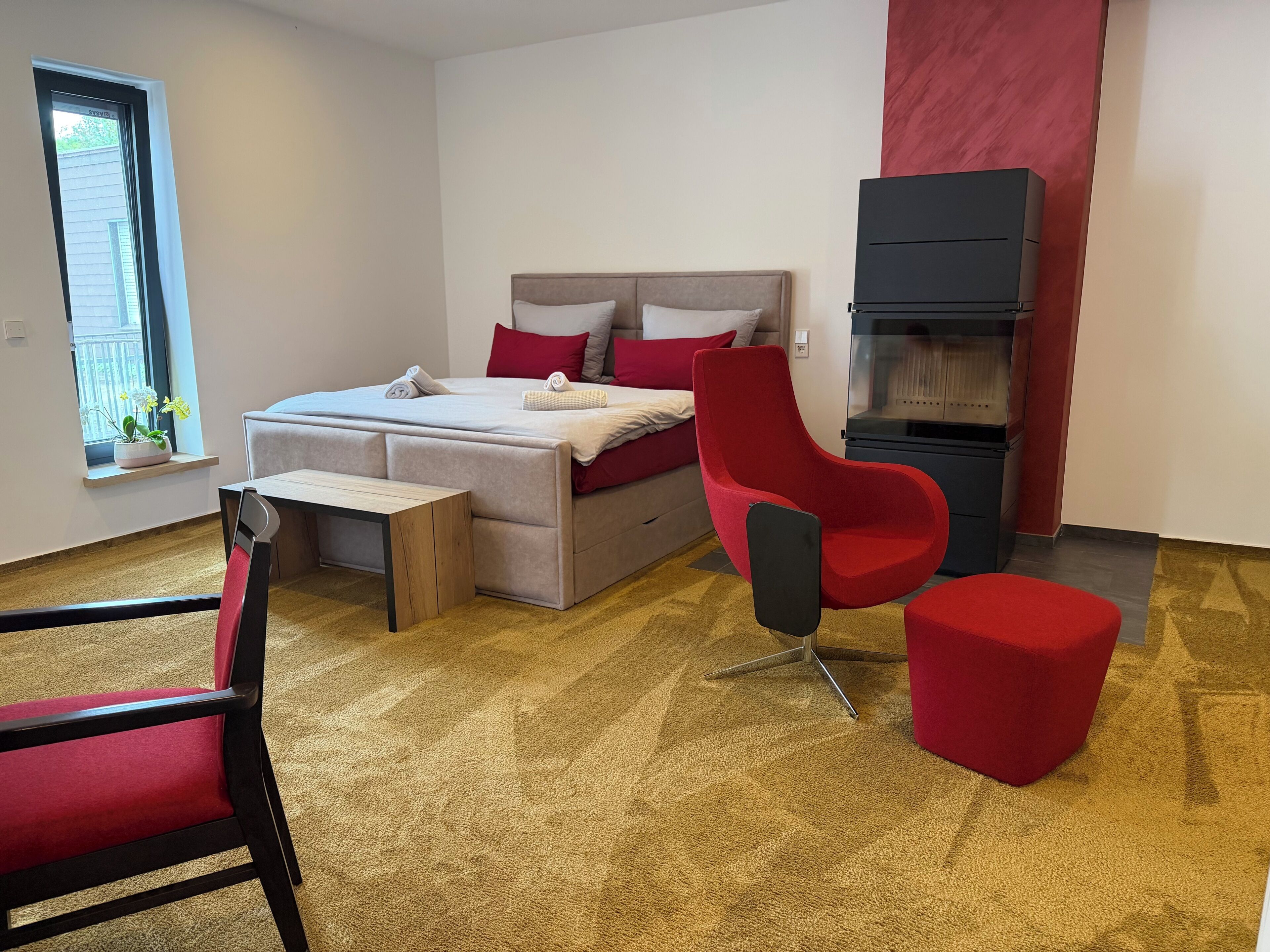 Ein modernes Schlafzimmer mit einem Bett, einem roten Sessel, einem kleinen Tisch und einer eingebauten schwarzen Kommode.