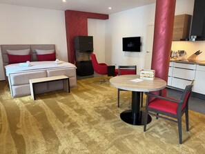 Habitación de hotel con cama, escritorio, silla, televisor y kitchenette.
