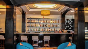 Eine Bar mit Regalen voller Spirituosenflaschen, blauen Stühlen und einem runden Tisch mit einer Lampe.