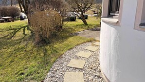 Un chemin menant à un bâtiment bordé de pierres, entouré d’herbe et d’arbres.